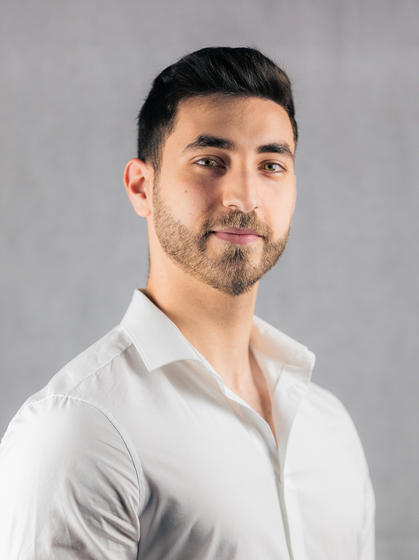 Photo of Mohammed Saffouri, wearing a white shirt, slightly in profile but with his face turned to the camera, against a grey background.
